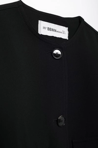 Detail of minimalist round neckline, woven fabric texture, and resin buttons on black jacket