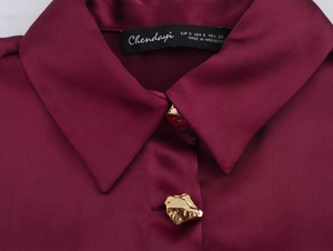 Detail of burgundy satin shirt fabric texture and golden irregular hammered metal buttons