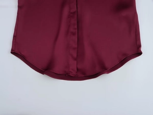 Detail of burgundy satin shirt featuring curved hem and precise stitching on silk texture