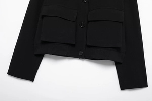Detail of black cropped jacket featuring large flap pockets and ribbed hemline