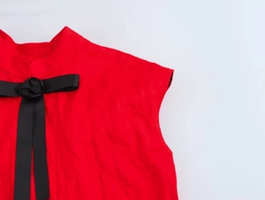 Gros plan d'une robe rouge sans manches avec nœud noir et fleur en tissu