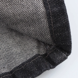 Gros plan du tissu denim foncé montrant le tissage en sergé et les détails de couture