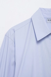 Détail du col d'une chemise rayée bleu clair avec coutures précises et étiquette intérieure