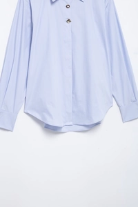 Détail d'une chemise bleu clair avec des boutons dorés décoratifs et texture rayée