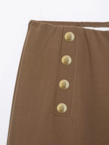 Macro detail of brown high-waist pants with golden crest buttons and elastic waistband