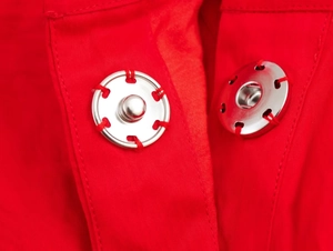 Détail du bouton-pression argenté sur robe rouge plissée avec coutures visibles