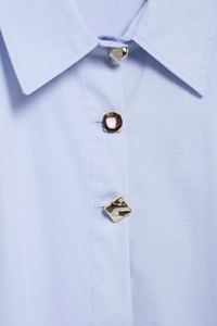 Détail des boutons métalliques et écailles de tortue sur une chemise rayée bleu clair
