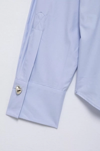 Détail de la manche d'une chemise bleu clair avec un bouton métallique argenté en cœur