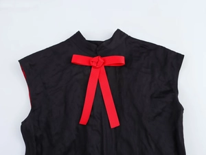 Détail d'une robe noire sans manches avec nœud en ruban rouge côtelé au col montant