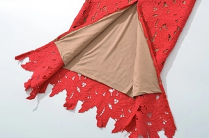 Close-up of elegant red floral lace fabric with a smooth beige lining and scalloped hem