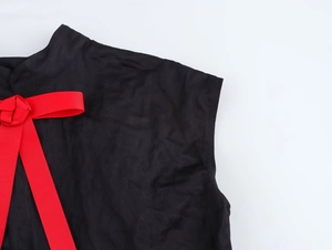 Détail d'une robe noire sans manches avec un nœud côtelé rouge sur le col