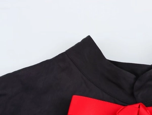 Détail d'un nœud côtelé rouge sur une robe à col officier noir avec tissu texturé