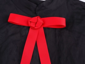 Détail du nœud en ruban gros-grain rouge sur l'encolure noire texturée d'une robe