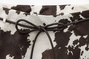 Gros plan sur le tissu imprimé vache avec une fine ceinture en cuir marron nouée