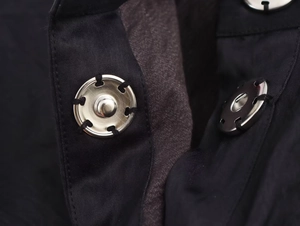 Détail du bouton-pression en métal argenté sur robe noire avec couture à six trous