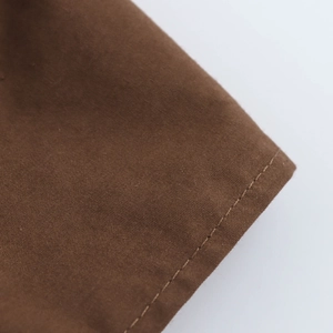 Detailed view of brown fabric with smooth plain weave texture and neat stitching seams