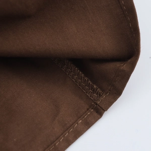 Macro detail of the double-stitched hem and fine edge sewing on the dark brown dress