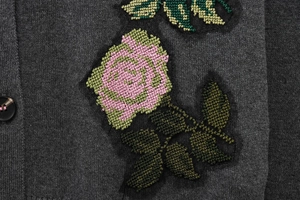 Gros plan d'un gilet gris en maille avec broderie florale rose et détail de bouton noir
