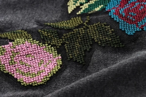 Gros plan de broderie florale colorée au point de croix sur maille foncée épaisse