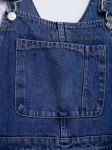 Detail of deep blue denim overalls featuring orange stitching and functional chest pocket