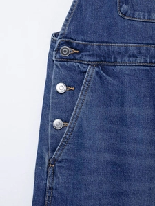 Detail view of dark blue denim overalls featuring contrast stitching and metal buttons