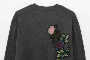 Détail de la broderie rose et de la maille sur le dos d'un cardigan gris foncé
