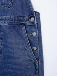 Detail of dark blue denim overalls featuring orange stitching and silver metal buttons