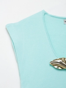 Dettaglio del top in maglia verde menta con scollo a V e decorazione in metallo dorato