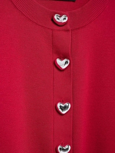 Détail d'un cardigan en tricot rouge avec boutons métalliques argentés en cœur