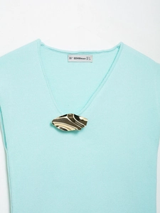 Dettaglio del top in maglia azzurro con scollo a V e fibbia in metallo dorato ondulato