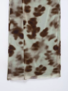 Detail shot of sheer mint green mesh fabric featuring brown abstract tie-dye print patterns