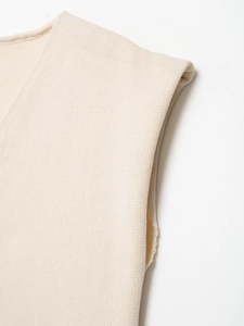 Dettaglio ravvicinato della maglia beige con trama fine e accenti con fibbia metallica