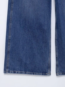 Close-up of dark blue denim fabric with orange contrast stitching and hem detail