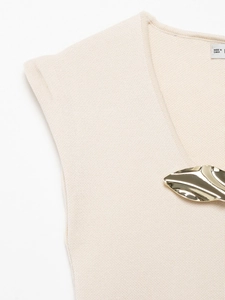Dettaglio di gilet in maglia beige con fibbia in metallo dorato e trama con scollo a V