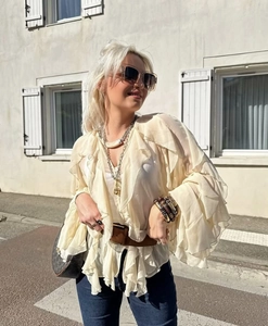 Close-up of cream v-neck ruffled blouse with layered chiffon sleeves and bohemian accessories