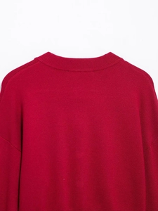 Détail du pull en maille rouge montrant le col rond côtelé et la couture d'épaule tombante