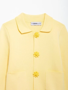 Close-up of yellow knit cardigan featuring 3D floral buttons and woven brand neck label