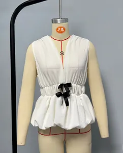 Detail of white sleeveless V-neck textured top with black bow accents and peplum waist