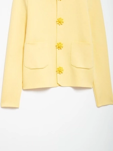 Detailed view of floral buttons and knitted texture on light yellow cardigan jacket