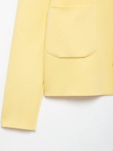 Detailed close-up of light yellow knitted cardigan fabric texture and large pocket design