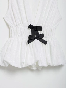 Detail view of white pleated fabric with elastic waist and two black satin bows