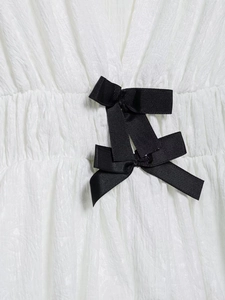 Detail of white pleated fabric with two contrast black ribbon bows on the waistline