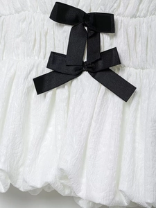Close-up of white textured fabric with a black grosgrain ribbon bow detail