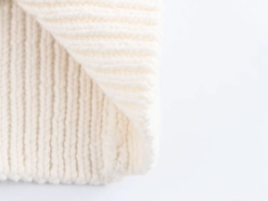 Détail macro de la texture en maille côtelée épaisse de ce gilet en coton blanc crème