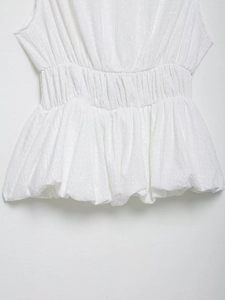 Detailed macro view of white sleeveless top showing elastic smocked waist and textured fabric