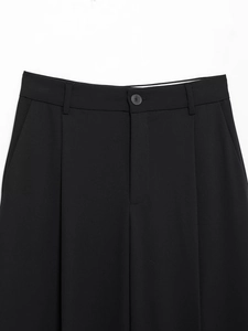 Detail of black wide-leg trousers showing waistband, button closure, and front pleats