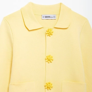 Pale yellow knit cardigan featuring 3D floral buttons and small collar on white background