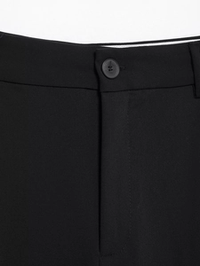 Detailed close-up of the waistband featuring a matte black button on tailored black trousers