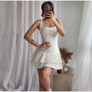 Detail shot of the white sleeveless pleated mini dress with a square neckline on a model