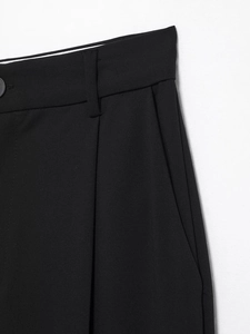 Detail of black wide-leg trousers showing waist pleats, pockets, and twill fabric texture